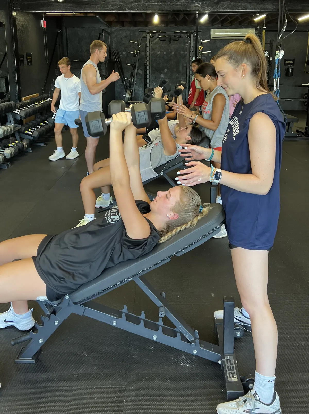 12U & 14U Softball athlete pressing dumbbells with a teammate spotting
